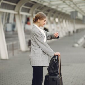 Cheerful female manager checking time on wristwatch standing with bags near bus station